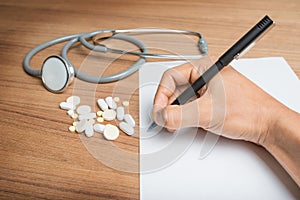 Hand with pen over blank paper form with stethoscope and pills