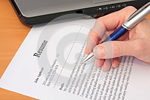 Hand with Pen Proofreading a Resume by Laptop photo