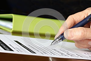 Hand with Pen Signing Form by Green Folder