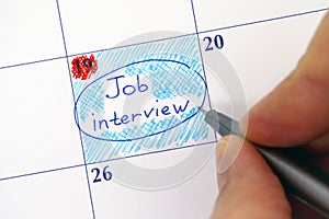 Hand with pen writing reminder Job Interview in calendar