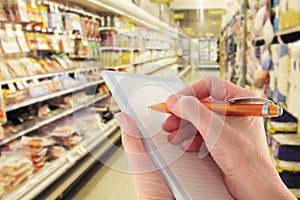 Hand with Pen Writing Shopping List in Supermarket