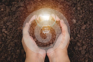 Hand of person holding light bulb with soil for idea, success