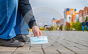 Hand of a person, a man who picks up a discarded medical antibacterial breathing mask from the ground, from the road