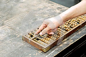 Hand of person playing and demonstration used of ancient Chinese abacus on old black wooden table