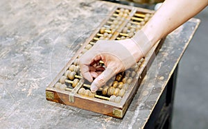 Hand of person playing and demonstration used of ancient Chinese abacus on old black wooden table