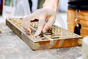 Hand of person playing and demonstration used of ancient Chinese abacus on old black wooden table