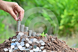 Hand of person put the coin on stack coins on the soil and nature background