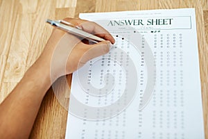 Hand of person, test and answer sheet on table for exam, education and student writing quiz in college. Assessment