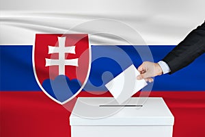 Election in Slovakia. The hand of man putting his vote in the ballot box. Waved Slovakia flag on background.