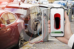 Hand with phone on a background of electric car charging point.