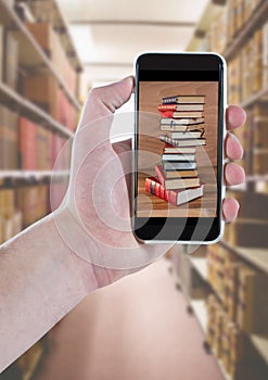 Hand with phone showing book pile against blurry bookshelfs