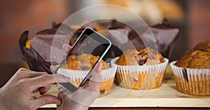 Hand photographing muffins through smart phone at bakery