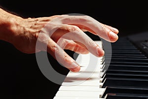 Hand of pianist play the keys of the digital piano on black background close up