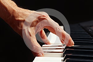 Hand of pianist play the keys of the electronic synth on black background close up
