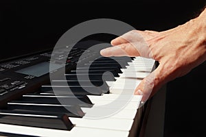 Hand of pianist playing the electronic synthesizer on black background