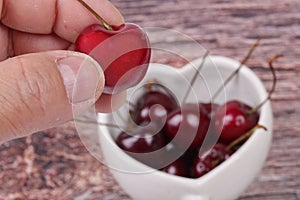 Hand-picked cherriy and cherries in heart-shaped mug on wooden.