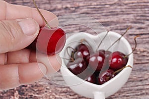 Hand-picked cherriy and cherries in heart-shaped mug on wooden.