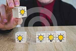 Hand picked a wooden cubes with the yellow light bulb symbol on wooden table. New idea, Innovation and Solution concepts