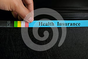 Hand picking health insurance file record in black binder folder. Health insurance benefit concept.