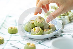 Hand picking Matcha Green Tea Cookies Singapore or Matcha Green Tea cashew Cookies with dried flower blurred on green vintage