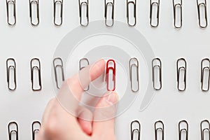 Hand picking among metal paperclips one red, different from others