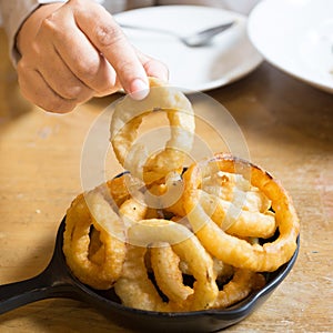 Hand picking Onion rings in black plate on the wood table in restaurant