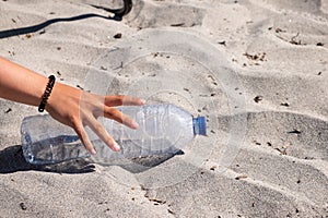 a hand picking up an empty plastic bottle from the sand on the beach, ecology concept