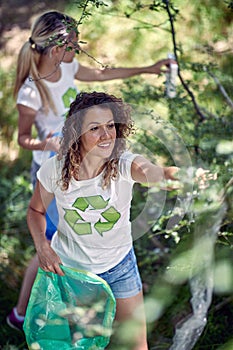 Hand picking up garbage and plastic for cleaning park or forest. Women in white shirts on sunny day collecting trash in bag.