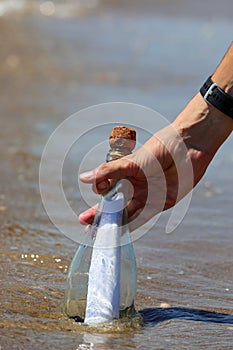 hand picking up glass bottle with message from sea