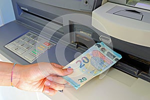 Hand picking up money in European banknotes from an ATM bank cash machine