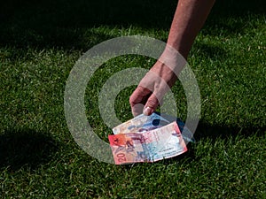 Hand picking up money from the ground. swiss currency. grass ground