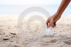 A hand picking up a plastic glass trash on the beach