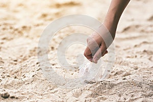 A hand picking up a plastic glass trash on the beach