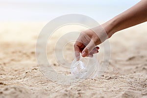 A hand picking up a plastic glass trash on the beach