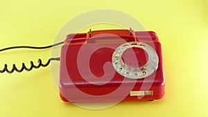 hand picks up red landline phone on yellow background. Old vintage home phone with wires and rotary dialer. Conversation