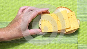 The hand picks up a sandwich of white bread with slices of hard cheese