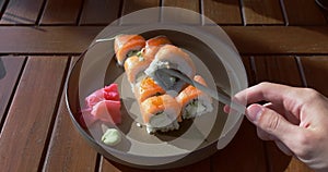 Hand picks up sushi using chopsticks. Amazing tasteful appetizing sushi in rays of bright sun, daytime morning lighting