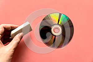 Hand pinching rubber over light reflected compact discs CD or digital versatile disc DVD on the pink paper background.