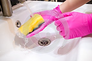 A hand in a pink glove washes a washbasin in the bathroom with a sponge with detergent