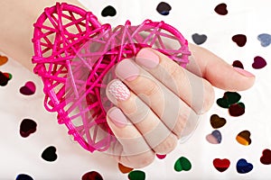 Hand with pink matte manicured nails holding a heart