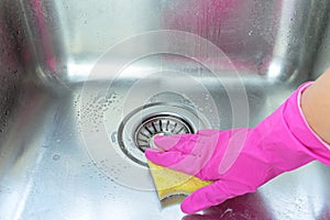 Hand in pink rubber glove clean stainless steel sink with sponge