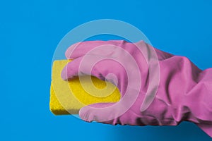 A hand in a pink rubber glove holds a yellow sponge.