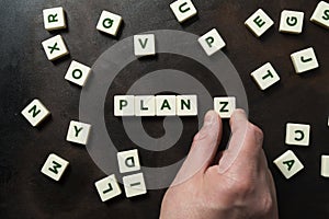 A hand places the letter Z next to the word PLAN