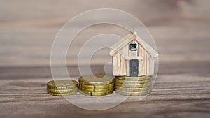 Hand places a miniature house on stacks of coins