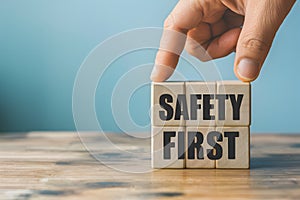 Hand places wooden block with SAFETY FIRST on blue background, promoting security