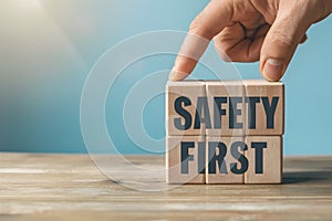 Hand places wooden block with SAFETY FIRST on blue background, promoting security