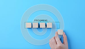 Hand places wooden cubes arranged in row on blue background. with the word progress. in progress, work loading bar, achievement