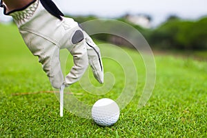 Hand placing golf-ball on tee over beautiful golf