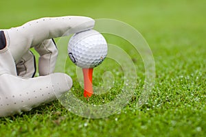 Hand placing golf-ball on tee over beautiful golf