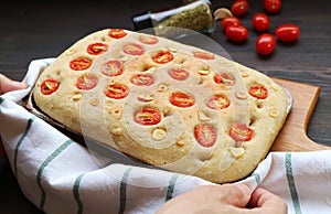 Hand Placing Italian Tomato and Garlic Focaccia Bread on Wooden Breadboard
